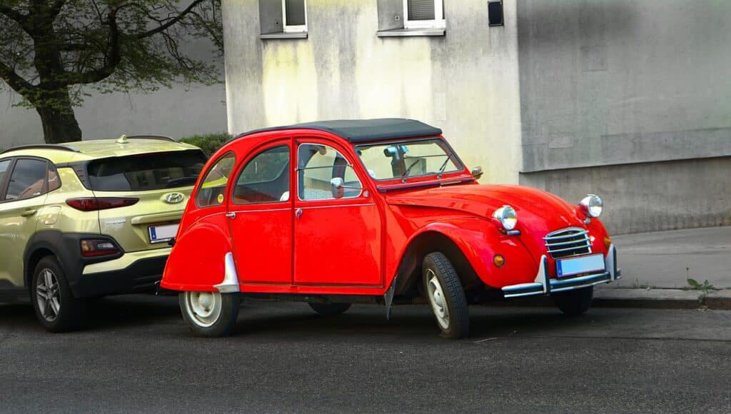 Rotes Oldtimer-Auto parkt neben modernem Wagen.