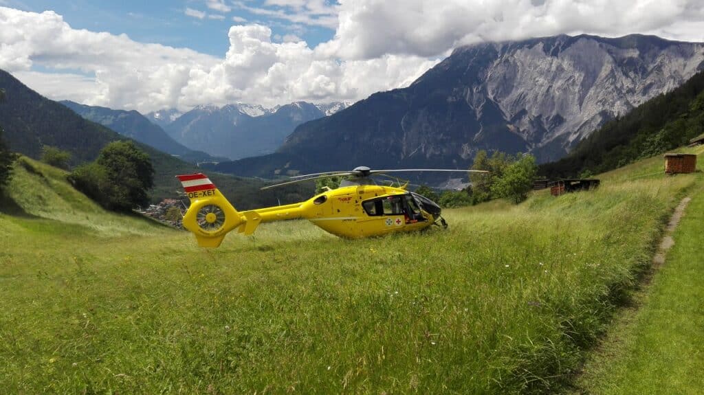 Rettungshubschrauber landet auf einer Wiese in den Bergen.