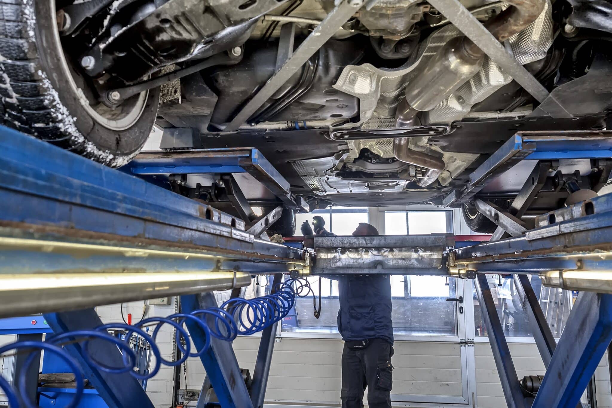 Mechaniker prüft in einer Werkstatt den Unterboden eines Autos auf der Hebebühne